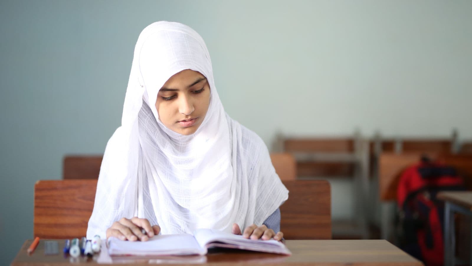 A school student in a hijab reading at her desk